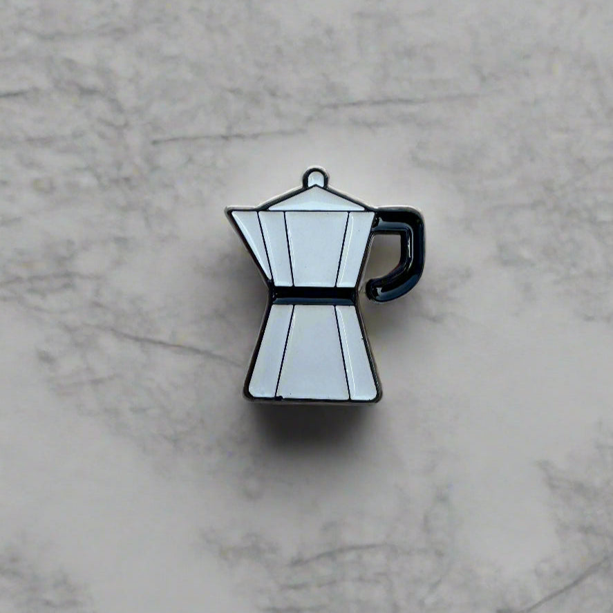 Enamel pin of a coffee pot on a marble surface