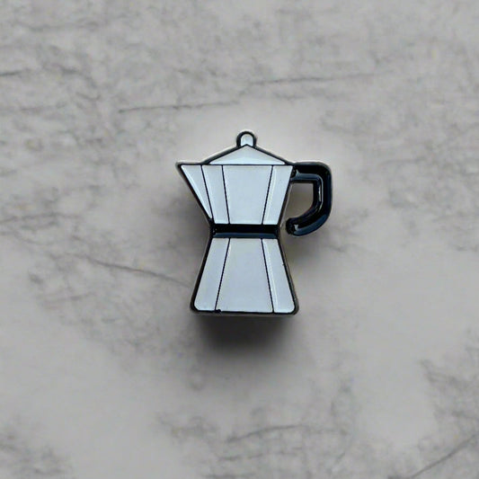 Enamel pin of a coffee pot on a marble surface